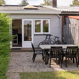 Veranda von 3 in einer Reihe Ferienhaus in Renesse, Schouwen-Duiveland, Zeeland mit Gartenmoebeln und gruener Umgebung.