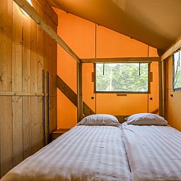 Gemuetliches Schlafzimmer in Safaritent 8, einer Glamping-Lodge in Vrouwenpolder, Walcheren, Zeeland, mit Holzakzenten und natuerlichem Licht.