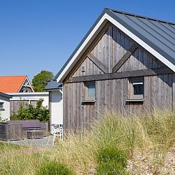 L6B Komfort-Ferienhaus in Nieuwvliet-Bad, Zeeland mit Holzfassade und Terrasse, umgeben von Duenen und Natur.