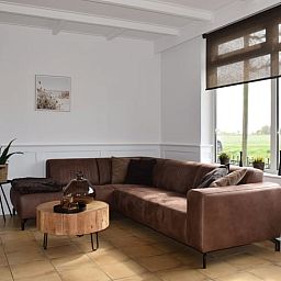Stilvolles Wohnzimmer im Ferienhaus in Schoondijke, Zeeuws-Vlaanderen, mit einem bequemen braunen Ledersofa und Blick auf die natuerliche Umgebung.
