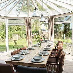 Lichte eetkamer in Vakantiehuis in Sluis, Zeeuws-Vlaanderen, met uitzicht op groene tuin. Perfect voor een ontspannen verblijf in Zeeland.