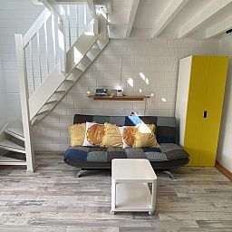 Modernes Wohnzimmer im Ferienhaus VZ991 in Ouddorp, mit hellen Moebeln und Treppe.