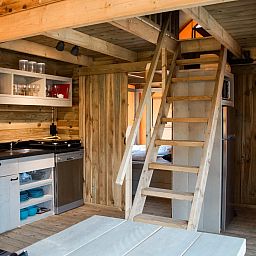 Gemuetlicher Innenbereich des Safarizeltes Duinroos in Ouddorp, Goeree-Overflakkee, mit Holzinterieur und moderner Kuecheneinrichtung.