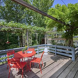 Veranda von Huisje Joep in Goedereede, schoene Terrasse mit roten Stuehlen, umgeben von Natur.