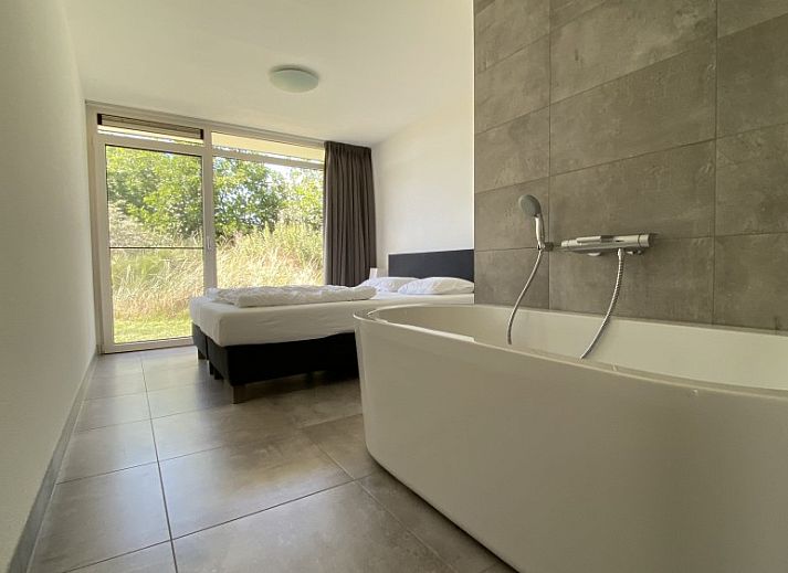 Veranda van Luxe 8 persoons Golf Villa Texel in De Cocksdorp met comfortabele stoelen en uitzicht op de groene tuin, perfect voor ontspanning.