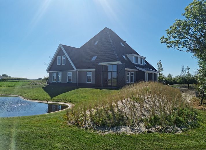 Vakantiehuis De Slufter in De Cocksdorp, Texel biedt een prachtig uitzicht op de natuur met een serene vijver en groene omgeving.
