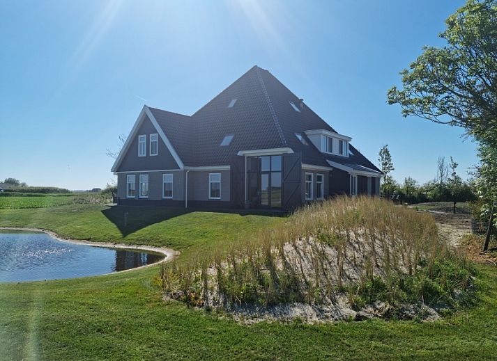 Vakantiehuis De Slufter in De Cocksdorp, Texel biedt een prachtig uitzicht op de natuur met een serene vijver en groene omgeving.