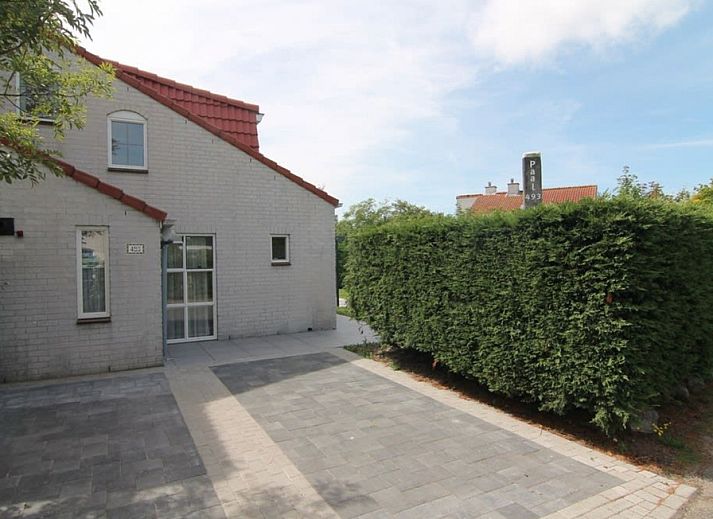 Vooraanzicht van Vakantiehuis D 493 in De Cocksdorp, Texel, met een ruime oprit en groene haag, ideaal voor een ontspannen verblijf op de Waddeneilanden.