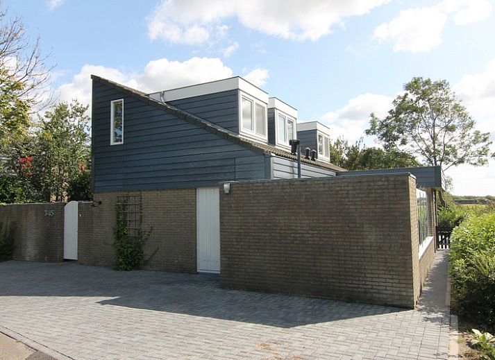 Vakantiehuis A 345 in De Cocksdorp, Texel biedt een zonnig terras met moderne tuinstoelen en een groene tuin, ideaal voor ontspanning.