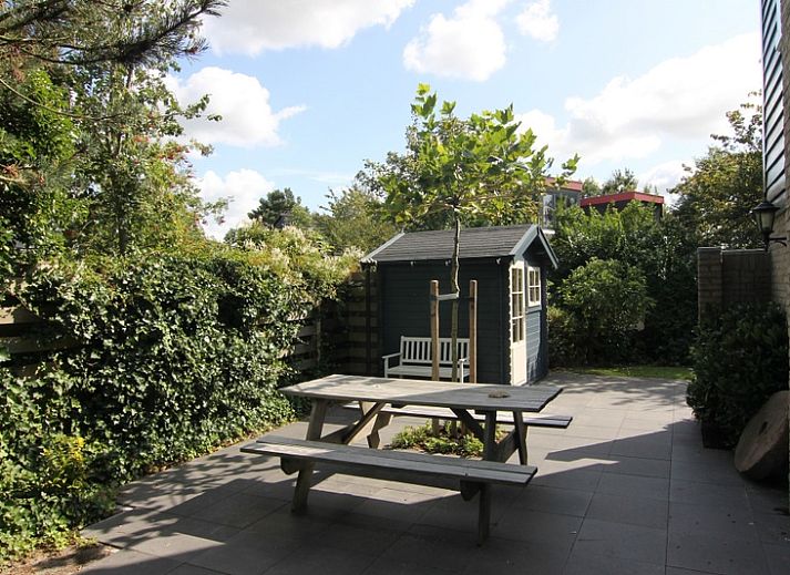 Vakantiehuis A 345 in De Cocksdorp, Texel biedt een zonnig terras met moderne tuinstoelen en een groene tuin, ideaal voor ontspanning.
