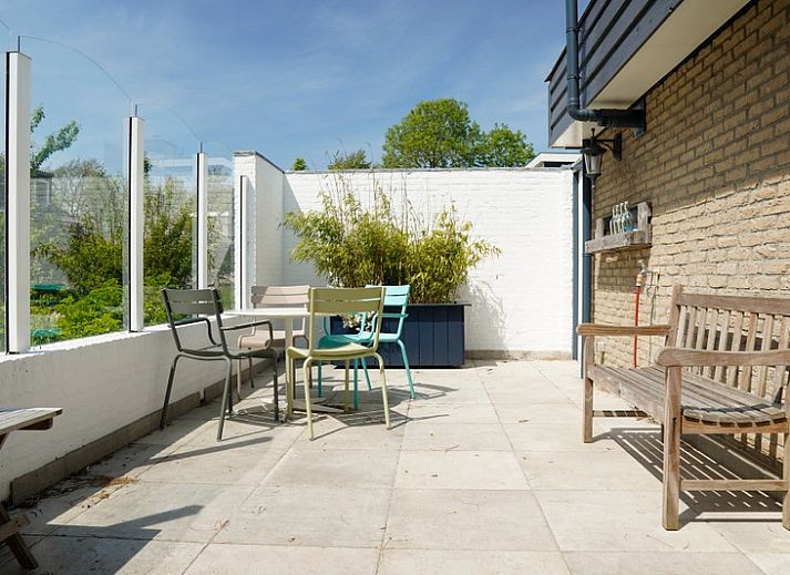 Vakantiehuis A 345 in De Cocksdorp, Texel biedt een zonnig terras met moderne tuinstoelen en een groene tuin, ideaal voor ontspanning.