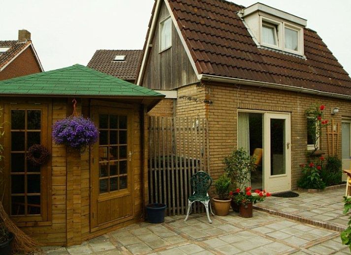 Ruhiger Aussenbereich des Ferienhauses Dunaa in De Koog, Texel, mit Holzschuppen und bluehenden Pflanzen.