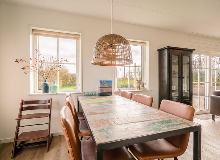 Gezellige woonkamer in De Zandhaas, vakantiehuis in De Koog, Texel, met uitzicht op de tuin en een sfeervolle houtkachel.