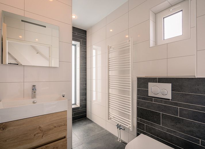 Gezellige woonkamer in De Zandhaas, vakantiehuis in De Koog, Texel, met uitzicht op de tuin en een sfeervolle houtkachel.