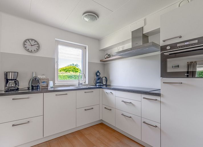 Sonnige Terrasse des Ferienhauses Honeysuckle 85 in De Koog, Texel mit Sonnenschirm und Gartenmoebeln.