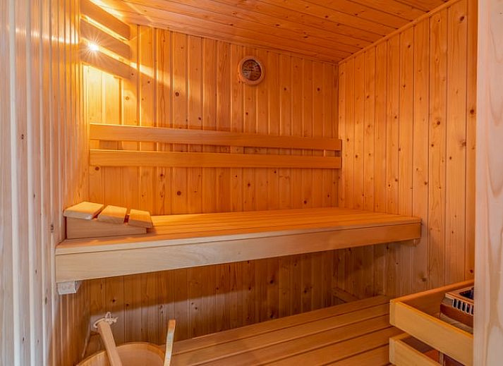 Blick aus dem Wohnzimmer des Ferienhauses in De Koog, Texel, mit gruenem Garten und gemuetlichen Sitzecken, ideal fuer einen ruhigen Urlaub.