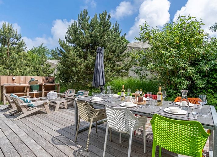Blick aus dem Wohnzimmer des Ferienhauses in De Koog, Texel, mit gruenem Garten und gemuetlichen Sitzecken, ideal fuer einen ruhigen Urlaub.