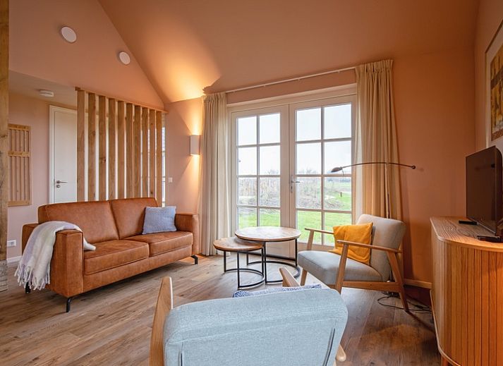 Gemuetliches Wohnzimmer im Ferienhaus Kamille in Den Hoorn auf Texel mit komfortabler Sitzecke und Blick auf die gruene Umgebung.