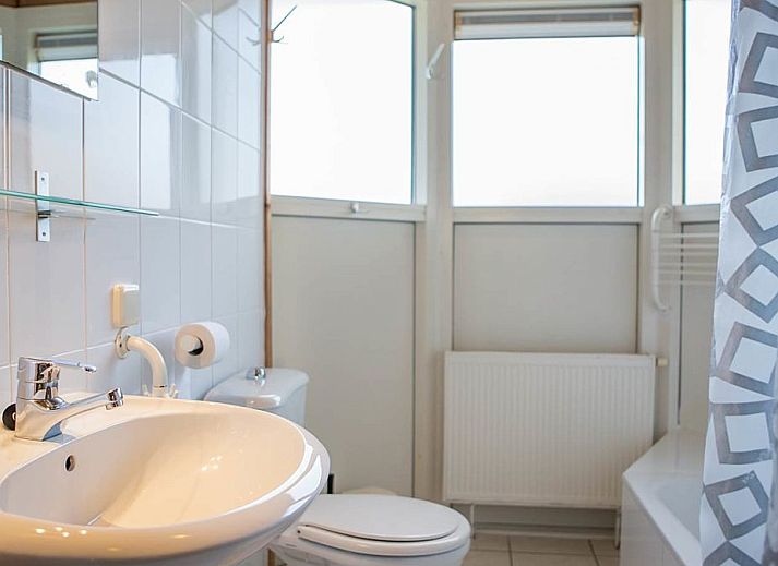 Gezellig terras met blauwe parasol bij Villabungalow, vakantiehuis in Oosterend, Terschelling, omringd door groene hagen op de Waddeneilanden.