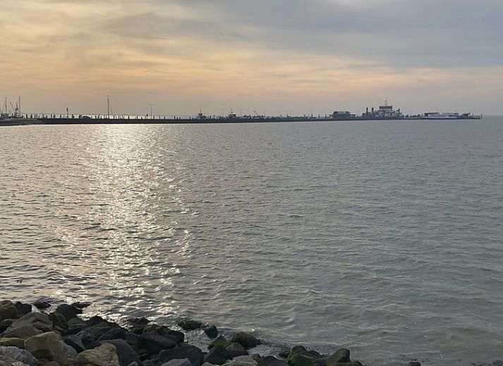 Comfortabele woonkamer in Vakantiehuisje in Buren Ameland met knusse bank en open keuken, ideaal voor ontspanning.