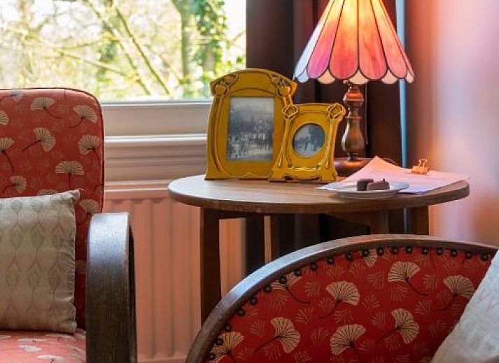 Zithoek met glas-in-lood ramen in B&B De Postoari Terschelling, Hoorn, biedt een sfeervolle plek om te ontspannen.