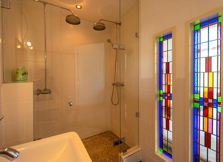 Zithoek met glas-in-lood ramen in B&B De Postoari Terschelling, Hoorn, biedt een sfeervolle plek om te ontspannen.