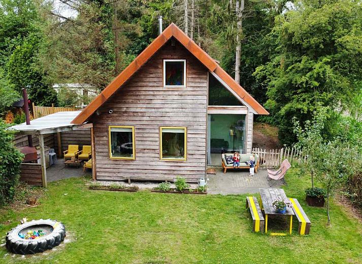 Gemuetliches Wohnzimmer des Ferienhauses DG588 in Midlaren, Drenthe, mit bunten Stuehlen und einem runden Esstisch.