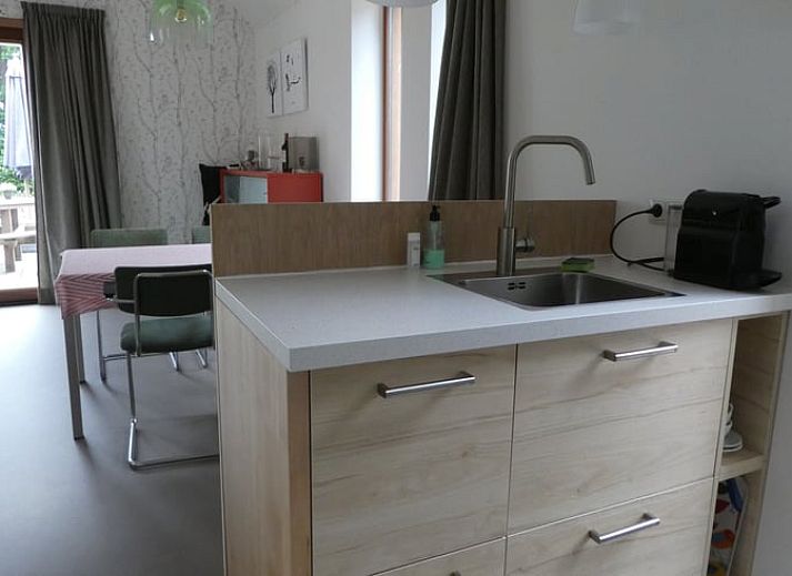 Veranda van Huisje in Bunne, vakantiehuis in Noord Drenthe, met houten terras, parasol en bloeiende geraniums, omgeven door groen landschap.