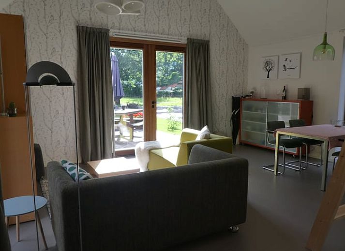 Veranda van Huisje in Bunne, vakantiehuis in Noord Drenthe, met houten terras, parasol en bloeiende geraniums, omgeven door groen landschap.