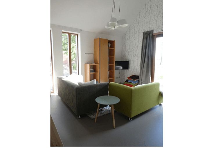 Veranda van Huisje in Bunne, vakantiehuis in Noord Drenthe, met houten terras, parasol en bloeiende geraniums, omgeven door groen landschap.