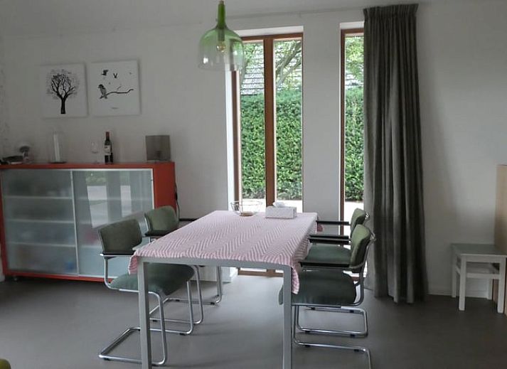 Veranda van Huisje in Bunne, vakantiehuis in Noord Drenthe, met houten terras, parasol en bloeiende geraniums, omgeven door groen landschap.