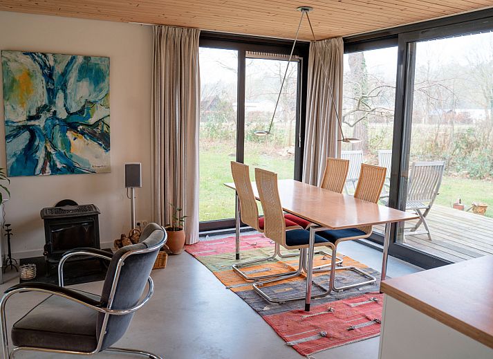 Terrasse des Ferienhauses DG357 in Meppen, Drenthe mit Holzstuehlen und gruener Umgebung.