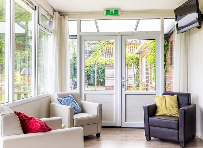 Gemuetliches Wohnzimmer im Ferienhaus Zonnehoek, Exloo, Drenthe mit Blick auf die gruene Natur durch grosse Fenster.