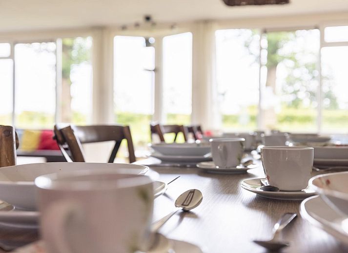 Gemuetliches Wohnzimmer des Ferienhauses Zonnehoek in Exloo, Drenthe, mit grosser Sitzecke und Blick auf die gruene Umgebung.