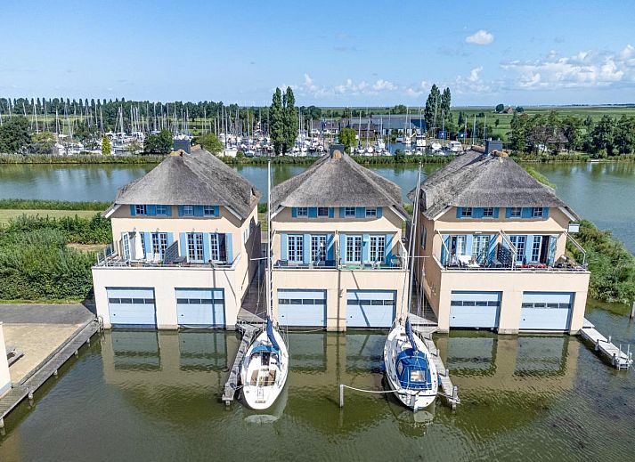 Luchtfoto van Schippershuis Stavoren, een vakantiehuis aan het water in Friesland, met aangemeerde zeilboot en rieten daken.