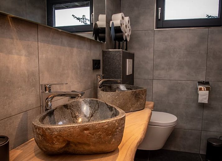 Gezellige woonkamer in Huisje in Empe, vakantiehuis Gelderse vallei, met stenen muur en comfortabele stoelen.