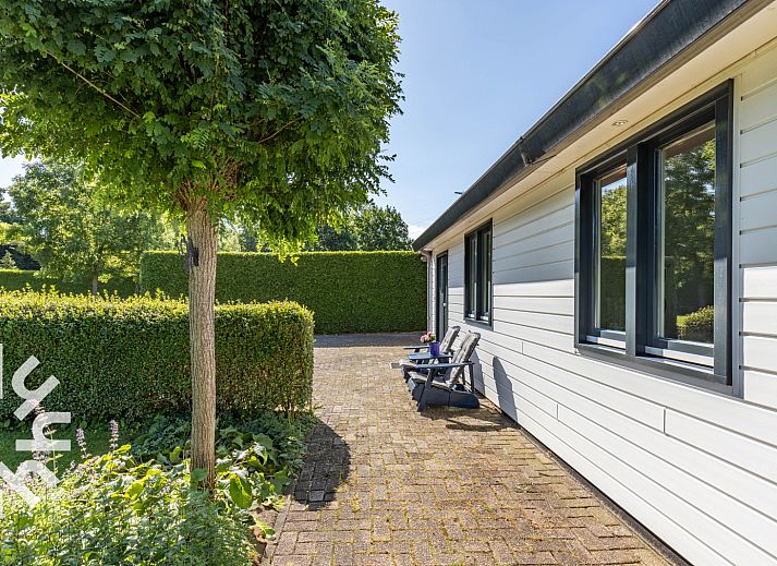 Geniet van de zonnige patio van vakantiehuis DG1560 in Ermelo, Veluwe, omgeven door weelderige natuur en rustgevende groene heggen.