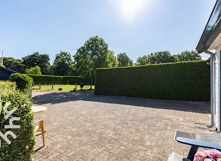 Geniet van de zonnige patio van vakantiehuis DG1560 in Ermelo, Veluwe, omgeven door weelderige natuur en rustgevende groene heggen.
