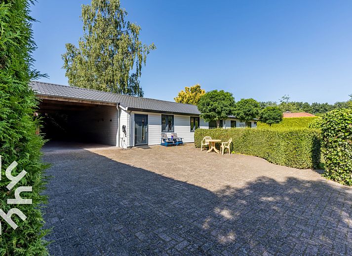 Geniet van de zonnige patio van vakantiehuis DG1560 in Ermelo, Veluwe, omgeven door weelderige natuur en rustgevende groene heggen.