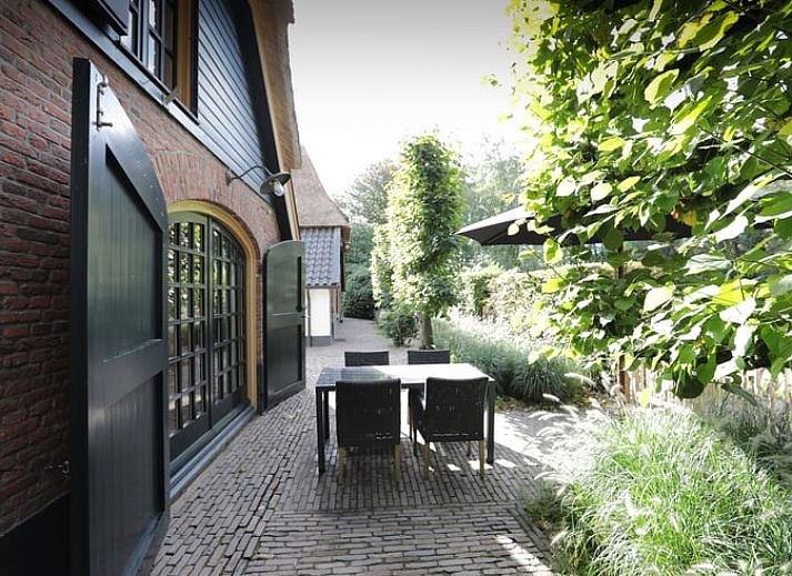 Cottage in Garderen, Ferienhaus in der Veluwe, Gelderland, umgeben von einer gruenen Hecke und einem Holztor.