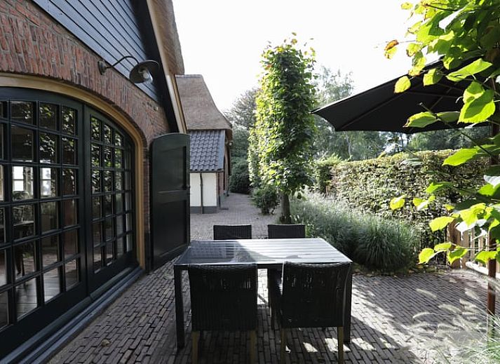 Cottage in Garderen, Ferienhaus in der Veluwe, Gelderland, umgeben von einer gruenen Hecke und einem Holztor.