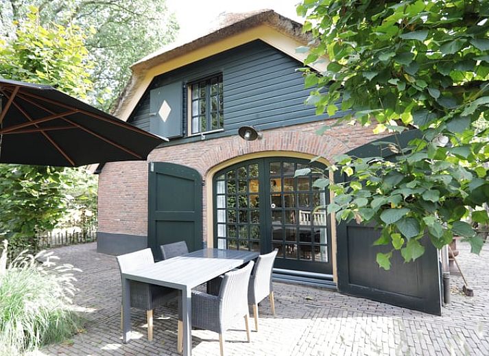 Cottage in Garderen, Ferienhaus in der Veluwe, Gelderland, umgeben von einer gruenen Hecke und einem Holztor.