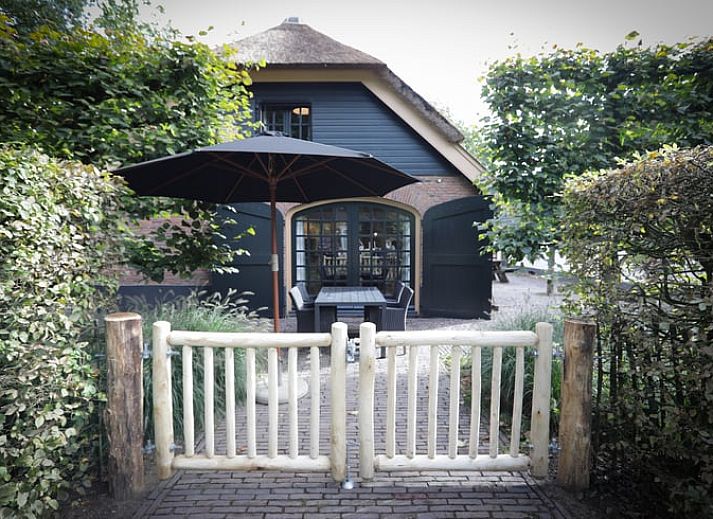 Cottage in Garderen, Ferienhaus in der Veluwe, Gelderland, umgeben von einer gruenen Hecke und einem Holztor.