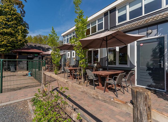 Terrace of vacation home Koolmees in Hulshorst, Veluwe with tables and umbrellas for relaxing outdoor seating.
