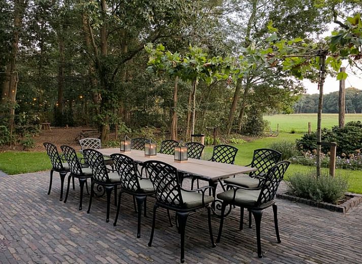 Elegante eetkamer in Huisje in Lunteren, Veluwe, met grote houten tafel en kroonluchter, ideaal voor familiediners.