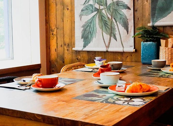 Gezellige eetruimte in Forest Hotel Den Helder, vakantie appartement met houten wanden en botanische prints.