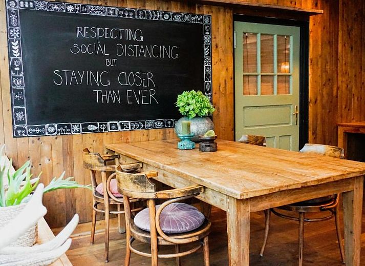 Gezellige eetruimte in Forest Hotel Den Helder, vakantie appartement met houten wanden en botanische prints.