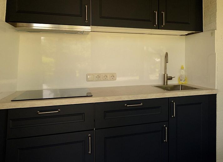 Sonnige Terrasse des Ferienhauses Korenwolf, Simpelveld, Suedlimburg mit Gartentisch und Sonnenschirm in gruener Umgebung.