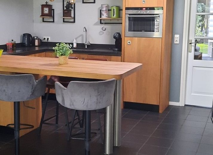 Terras met houten tafel en stoelen bij Grove Den in Sint-Oedenrode, Noord Brabant, omgeven door weelderige natuur.