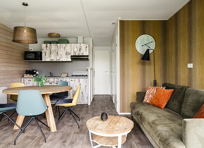 Gezellige woonkamer in Strandhuisje voor 5 personen, Julianadorp, Noordzeekust, met uitzicht op groene tuin en comfortabele zithoek.